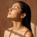 Gold-tone sunburst pendant necklace with thin chain, angled view